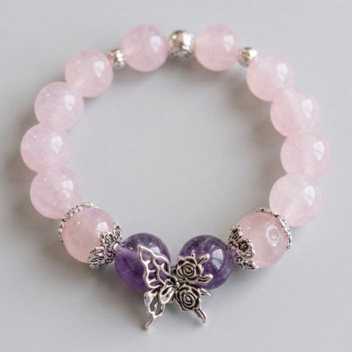 Beaded bracelet with pink and purple beads and a silver butterfly charm on a light gray background