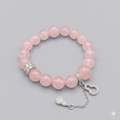 Pink beaded bracelet with silver chain and heart charm on a gray background